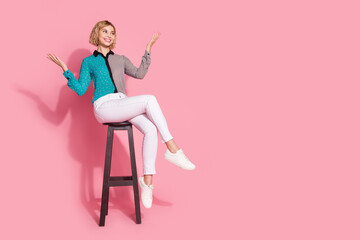 Full size photo of pretty girl model chair raise hands look empty space wear trendy striped cyan outfit isolated on pink color background