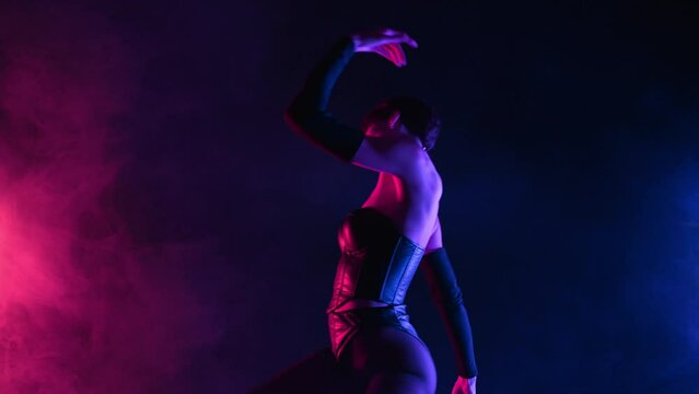 Sexy woman in bdsm leather corset performs dance moves in smoky neon light. Erotic hot fetish costume, mistress in dark studio. Dancer in night club