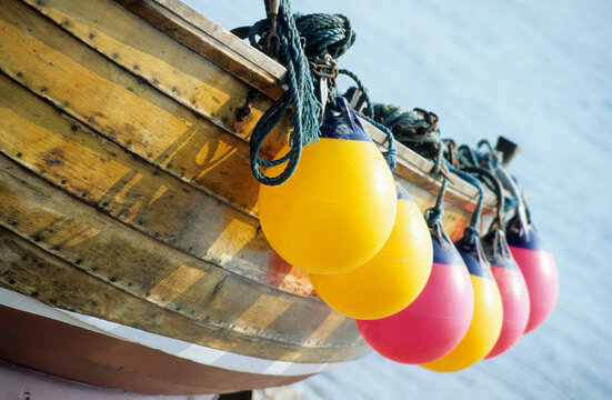 Horizontal image of yellow and red boat buoys hanging from the side of an old wooden boat. location Cromer Norfolk UK