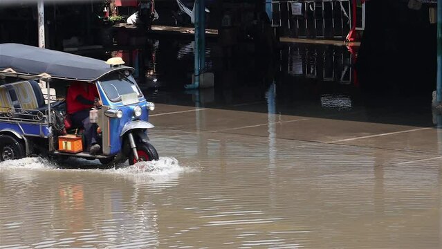 A traditional motorized tricycle - tuk tuk drives through a flooded street, Thailand