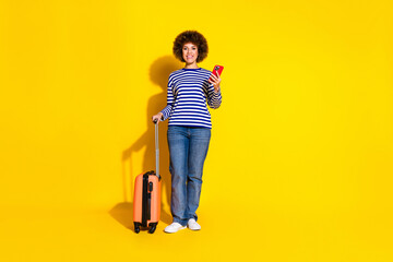 Full length photo of optimistic good mood woman dressed striped shirt holding valise smartphone isolated on yellow color background