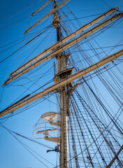 Tall ship mast, rigging, yards against clear sky. Classic sailing vessel with crow's nest, harking back to Age of Sail era