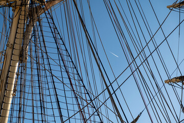 Nautical rigging on tall ship under clear sky with airplane contrail