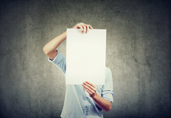 A young man holds a sheet of white paper in front of his face - 789259952