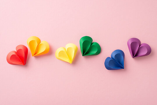 Diversity celebration vibe. Overhead shot of colorful heart symbols, representing varied relationships. Pastel pink canvas, ideal for social messages or ads