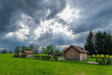 sun rays through the clouds, impressive weather atmosphere, next to a barn stands a tree, the single linden tree is dominant and towers over the hut. Dornbirn, Vorarlberg