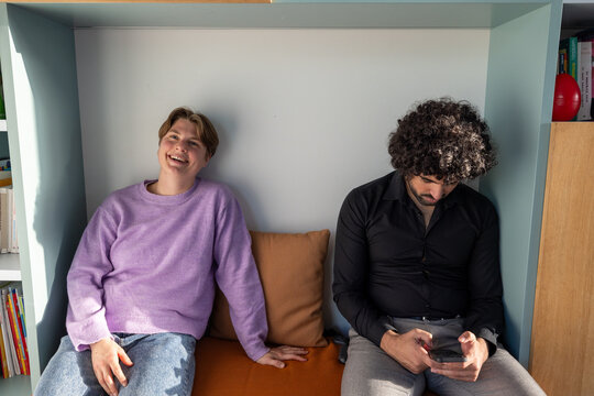 This photo captures the contrast of modern social interactions among friends. On one side, a person in a lavender sweater laughs heartily, while on the other, their friend with curly hair and a black