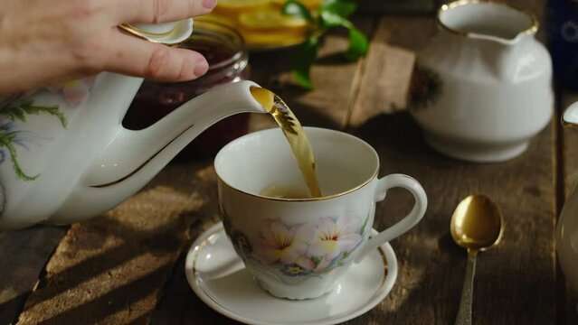 Pouring tea from teapot into porcelain cup. Morning breakfast.