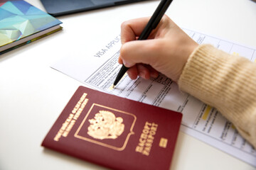 Close up of female hand filing out a visa application with a Russian passport