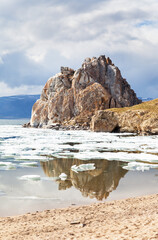 Baikal Lake on Spring. View of natural landmark of Olkhon Island - Shamanka Rock during ice drift on sunny May day. Sandy beach with reflection of rock near Khuzhir village. Scenic spring landscape