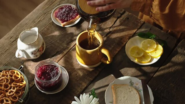 Tea time. Morning breakfast. Woman pours tea into mug and adds lemon slice