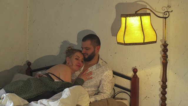 A man and woman are seen laying together under a lamp in bed.