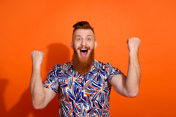 Photo of good mood lucky guy dressed print shirt screaming yes rising fists isolated orange color background