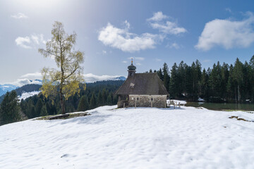 Little chapel in the mountains with great panoramic view over Bregenz forest. alpine scenery with alpine farmhouse and church on the hill. snowy landscape on the edge of forest