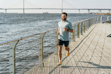A man runs with a smile on a boardwalk beside the river, a graceful cable-stayed bridge looms in...