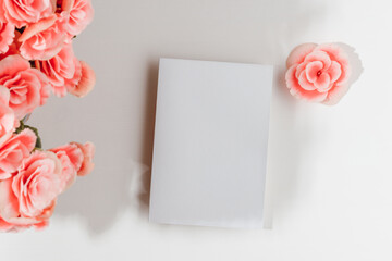 Paper sheet card with pink flowers and sunlight shadows on white wooden background. Card mockup with copy space for invitation, greeting, wedding and design. - obrazy, fototapety, plakaty