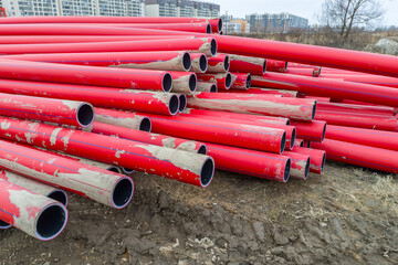 A pile of red pipes are stacked on top of each other. The pipes are made of plastic and are red in...
