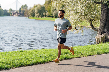 A beaming man enjoys a run by the lake, a bridge in the distance and trees in full bloom enhancing the scenic landscape.