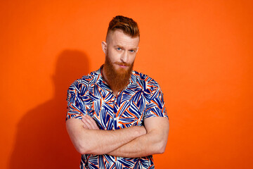 Photo of confident serious guy with red beard wear print shirt holding arms folded staring at you isolated on orange color background