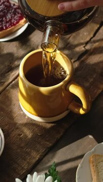Vertical video. Person pouring tea from teapot during morning breakfast.
