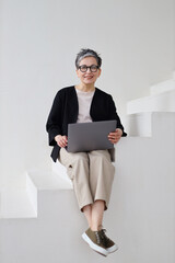 A mature pensioner woman embraces technology, working online with professionalism and joy from her...