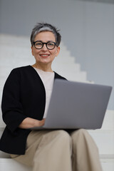 An entrepreneurial mature woman engages in online business from her modern office, blending...