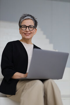 An entrepreneurial mature woman engages in online business from her modern office, blending technology with success.