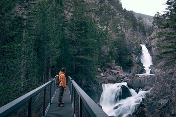 A man in an orange jacket standing in the middle of a bridge.