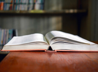 An open book or textbook vintage style on wooden table in the library and the bookshelves...