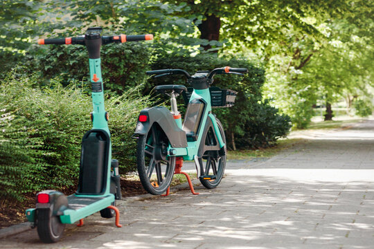Bike Sharing System and Scooter Rental Service in Green City. e-bicycle e-scooter parked in Sidewalk. Eco Transport concept. Green Background. Copy Space