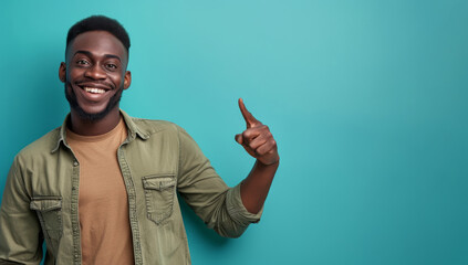 Happy black man in green shirt pointing upwards on a turquoise background