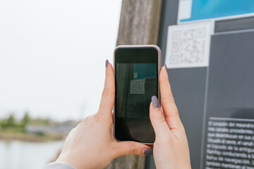 Detail of woman scanning a QR code on an information panel with her mobile phone