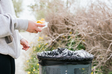 Detail of a woman throwing remains into a trash can during an outing in the countryside