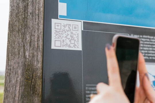 Detail of woman scanning a QR code on an information panel with her mobile phone - Powered by Adobe