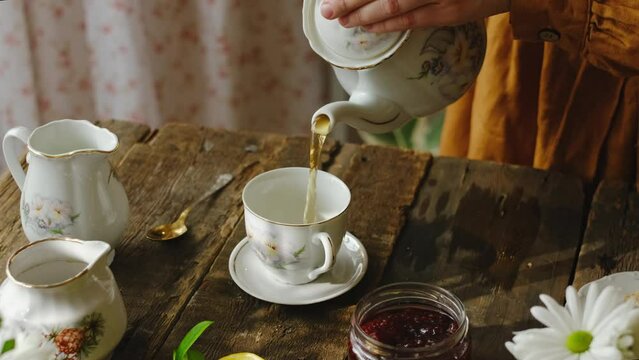 Pouring tea from teapot into porcelain cup. Rustic morning breakfast.