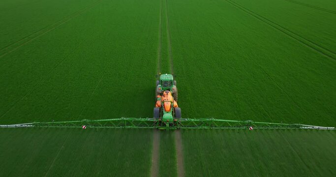 Aerial view of crop sprayer spraying pesticide on a soybean field at sunset. Drone shot flying over agricultural soybean field, tractor and crop sprayer protection plants to increase crop yield