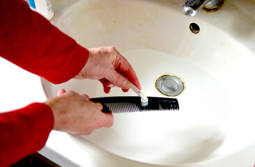 Person cleans the hair comb with an old disused toothbrush to remove the fatty residues from the...
