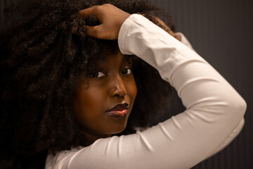 The intimate portrait features a Black woman with lush afro hair, wearing a white long-sleeved top....