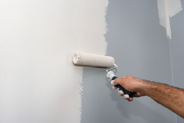 Painter paints a room in beige color using a paint roller at home.