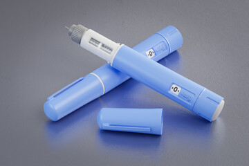 Two dosing pens of a fictitious Semaglutide drug used for weight loss (antidiabetic or anti-obesity medication) on a scratched metallic  background.