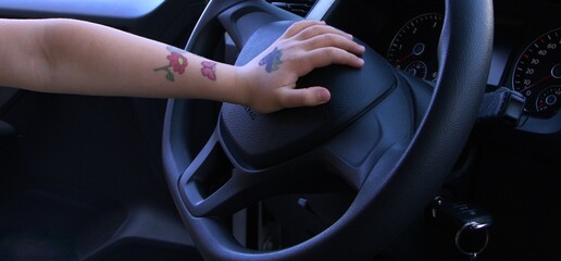 child's hand adorned with colorful tattoos resting casually on steering wheel in car. concepts:...