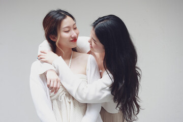 Two women in a gentle embrace, sharing an affectionate moment in a minimalist setting.