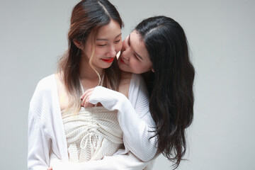 Two women in a gentle embrace, sharing an affectionate moment in a minimalist setting.