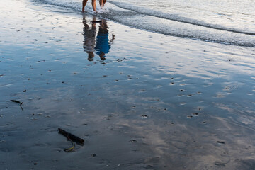 People walking on the beach near the sea during the late afternoon. Reflections in the water mirror.