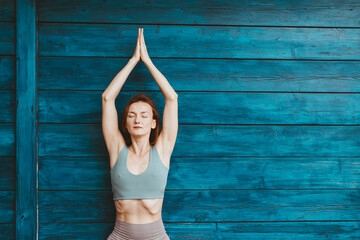 Woman practicing yoga on background of blue wooden wall.