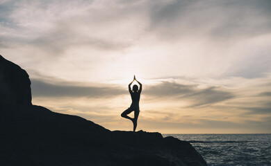 Silhouette woman in yoga pose on rock of the beach at sunset or sunrise. - 789344738