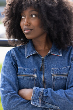A close-up portrays a Black woman with an afro, clad in a classic denim jacket, gazing away with a dreamy expression. The soft focus on her face enhances her contemplative look, suggesting deep