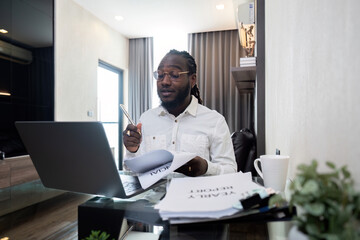 African American man working with laptop computer remote while sitting at glass table in living room. Black guy do freelance work at home office