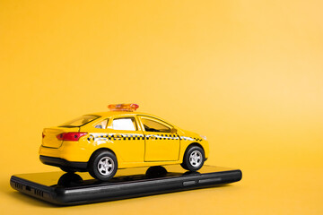 Urban taxi mobile online application concept. Toy yellow taxi car model. Hand holding smart phone with taxi service app on display. Mock up with copy space.