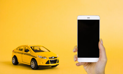 Urban taxi mobile online application concept. Toy yellow taxi car model. Hand holding smart phone with taxi service app on display. Mock up with copy space.